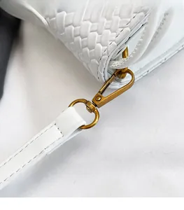Detailed close-up of premium gold metal hardware and woven leather texture on a white bag
