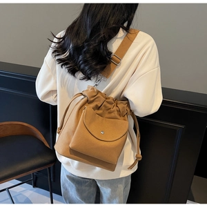 Brown canvas drawstring bucket bag with adjustable strap worn by a model in casual style