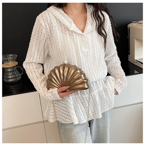 Détail d'une pochette dorée en forme de coquillage avec fermoir perle et chaîne