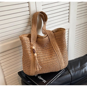 Detailed close-up of a large straw tote bag with woven texture and a wood bead tassel charm