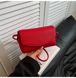 Detail of red pebbled leather crossbody bag with flap closure held by hand