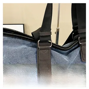 Close-up of denim tote bag showing leather reinforcement, metal buckle and nylon strap