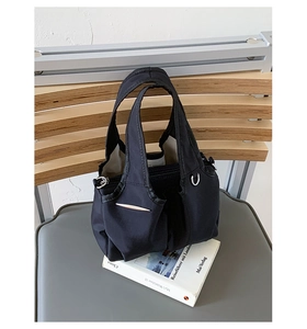 Detail of black nylon shoulder bag with silver hardware and smooth zipper on a white book