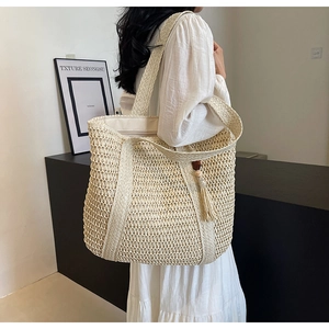 Detail of a large woven straw tote bag featuring a mesh texture and matching tassel charm