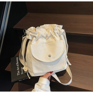 Detail of a minimalist cream canvas drawstring bucket bag with a snap-button front pocket