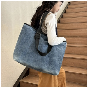 Detail of a large blue washed denim tote bag with black wide nylon shoulder strap