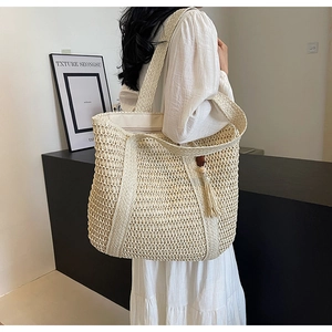 Detail of beige straw tote bag with tassels and zipper closure shown on shoulder