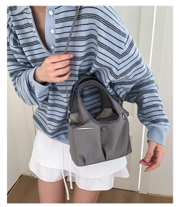 Detailed view of gray nylon tote bag with metal trim and adjustable strap on a model