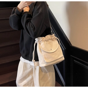 Detail of cream canvas drawstring bucket bag with front flap pocket on a shoulder strap