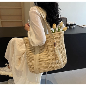 Detail of a beige straw tote bag with woven shoulder strap and vintage wood bead tassels