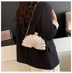Détail du sac de soirée coquillage blanc avec fermoir perle et fine chaîne dorée sur l'épaule