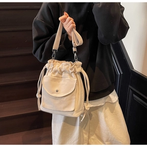 Detail of a beige canvas bucket bag with drawstring closure and magnetic flap pocket
