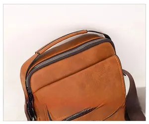 Detail view of the brown leather shoulder bag featuring a padded handle and dual metal zippers