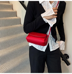 Close-up of a red textured leather crossbody bag with flap cover on a stylish model