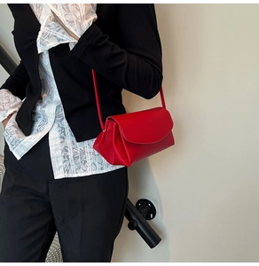 Close-up of red lychee grain leather shoulder bag with curved flap on a model