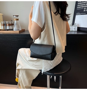 Detailed view of black litchi pattern square crossbody bag on model in a cafe setting