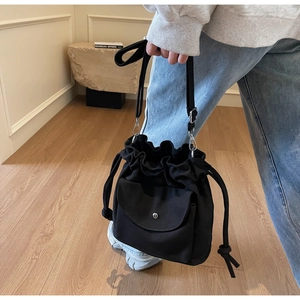 Detail of black canvas bucket bag with drawstring closure and front flap pocket on a model