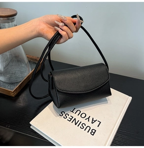 Detail of black lychee grain leather crossbody bag with rounded flap and slim strap