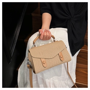 Detail of khaki woven handbag with leather straps and buckles on a wooden background