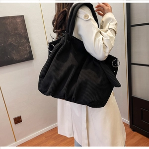 Detail of black corduroy shoulder bag with metal ring and knotted strap on model