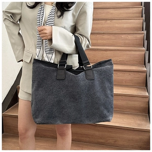 Large dark grey canvas tote bag held by a model on stairs for a casual commuting style