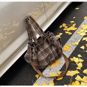 Close-up of brown checkered corduroy shoulder bag leaning against a car with autumn leaves