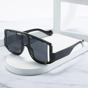 Oversized square sunglasses with gold rivets and black frames on a marble display