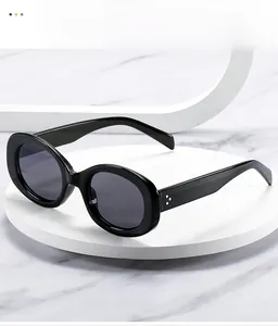 Detail of glossy black oval sunglasses with metal rivet accents on the thick frame