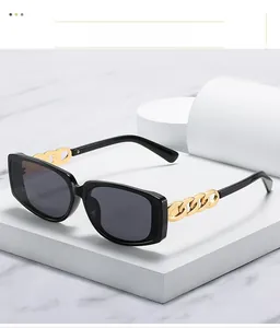 Close-up of black square sunglasses featuring chunky gold chain temples on marble block