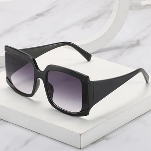 Lunettes de soleil carrées oversize avec monture noire et verres dégradés sur un socle blanc