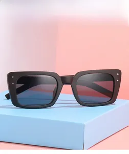 Vue détaillée de lunettes de soleil carrées noires avec rivets argentés sur boîte bleue