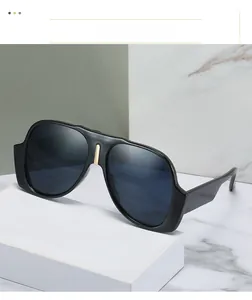 Detail of oversized black sunglasses with a gold metal bridge accent on a textured pedestal