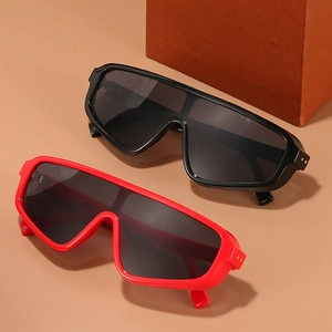 Oversized shield sunglasses in black and red with gold rivet details on warm background