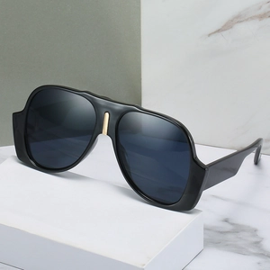 Oversized black aviator sunglasses with wide temples and gold bridge accent on pedestal