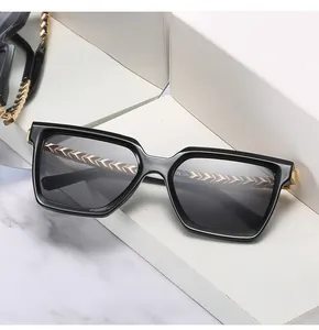 Close-up of oversized square sunglasses with gold metal temples and v-shaped engravings