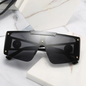 Oversized shield sunglasses with black frame and golden metal rivets on white marble