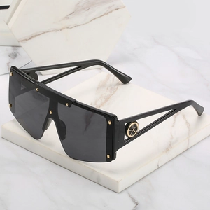 Oversized black shield sunglasses with gold rivets and cutout temples on marble