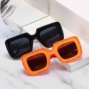 Lunettes de soleil carrées modernes en noir et orange texturé sur supports blancs