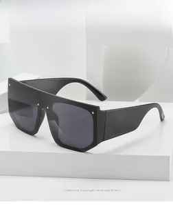Detail of black flat top sunglasses with gold rivet accents and wide temples on a white stand
