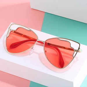 Cat eye sunglasses with gold wavy hollow metal frame and vibrant red lenses on podium