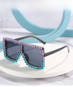 Close-up of oversized square sunglasses with purple and teal gradient rhinestone frames