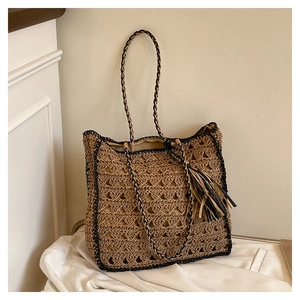 Detail of tan woven straw handbag featuring black contrast strap and decorative tassel