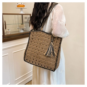 Detail of woven straw tote bag with black handles and decorative bicolor tassel
