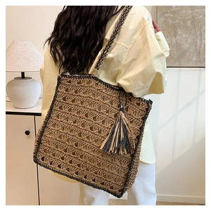 Detail of woven straw tote bag with contrast fringe tassels on a model's shoulder