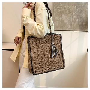 Detail of woven straw tote bag with black trim and tassel on shoulder