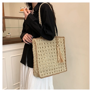 Detail of hand-woven straw tote bag with brown trim and tassel on a female model