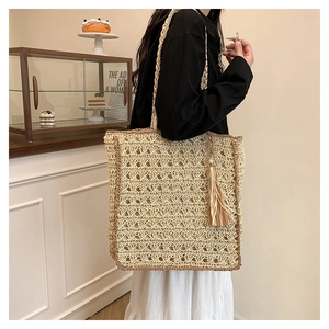 Detail of woven straw tote bag with elegant tassels and hollow weave pattern on a shoulder strap