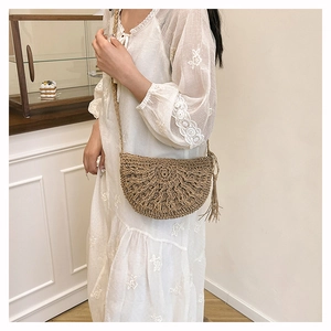 Detail of straw crescent crossbody bag with tassel and woven shoulder strap on model