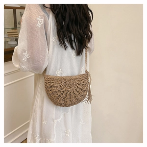 Detail of semi-circle straw crossbody bag with radial texture and tassel on a dress