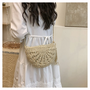 Detail of a minimalist cream straw crossbody bag with fringe trim on a model